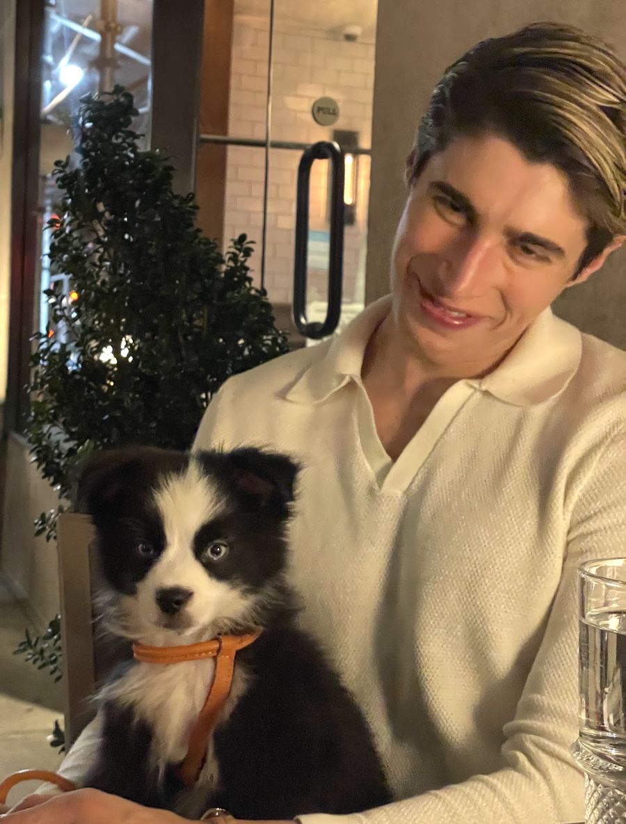 Fluffy smiling down at Charlie, who sits on his lap at a restaurant table wearing a tan leather harness